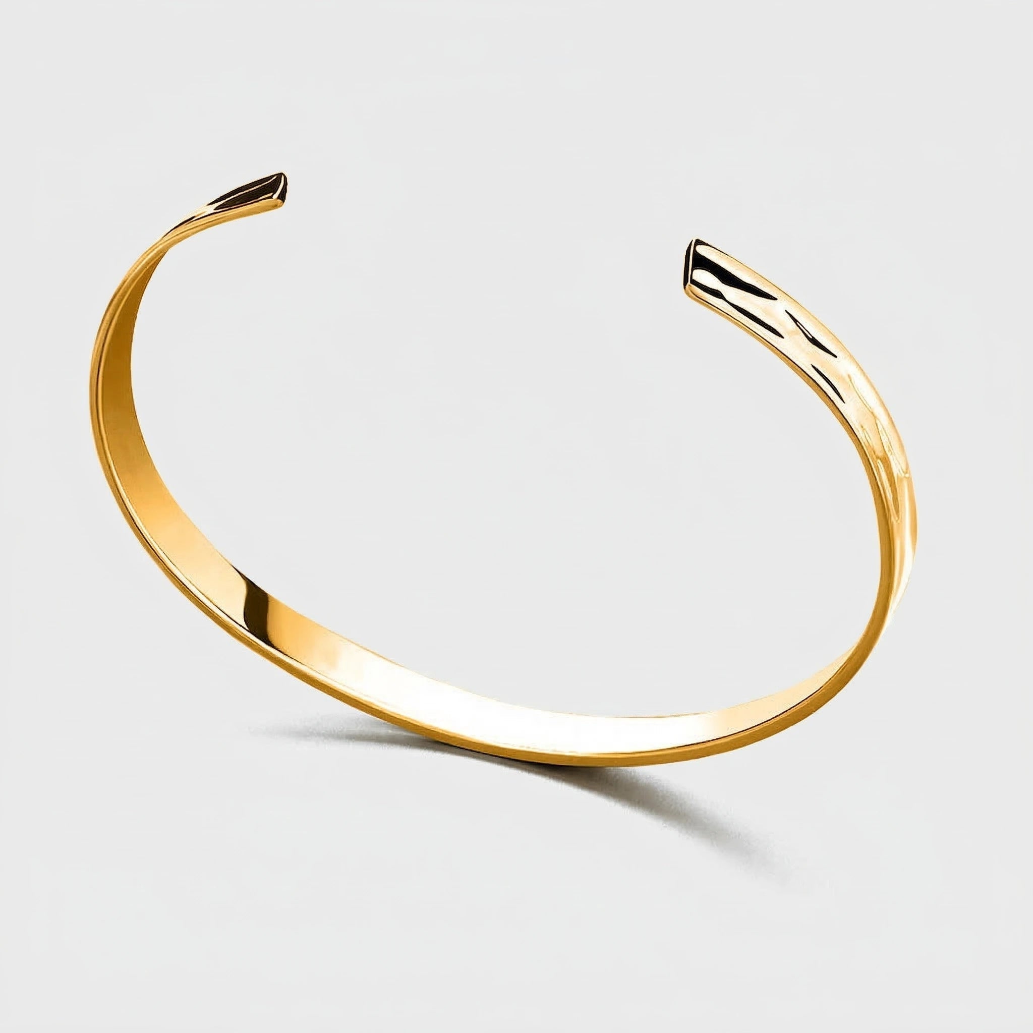 Gold tidal curve cuff bracelet on a light gray background