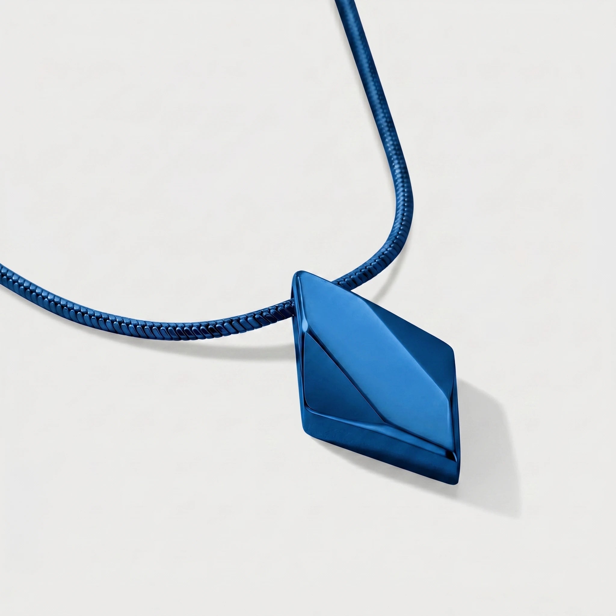 Blue geometric pendant on a thin blue cord against a light gray background