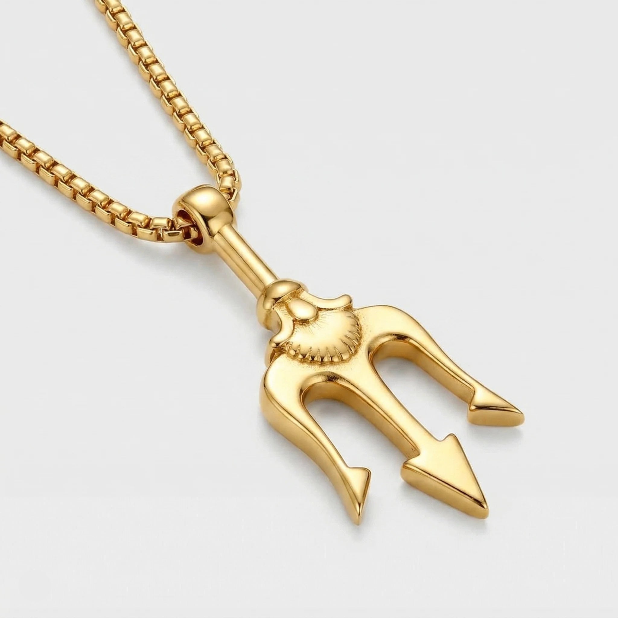 Gold trident pendant on a chain against a light gray background